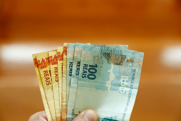 Mão segurando cédulas de real em texto sobre renda per capita.