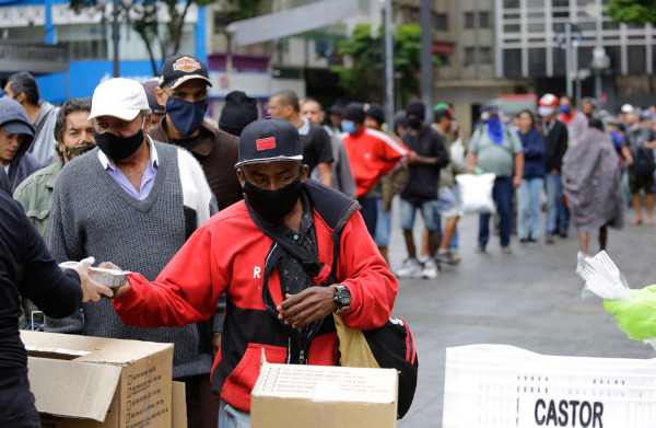 Fila de pessoas recendo mantimentos na pandemia, em texto sobre renda per capita.