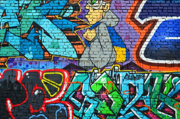 DJ manuseando aparelho em evento de hip-hop. Muro com grafite, tipo de pintura ligado ao hip-hop que é comum em muros e paredes em ambientes públicos.