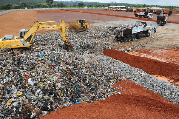Máquinas e caminhões trabalhando em um grande aterro sanitário. [imagem_principal]