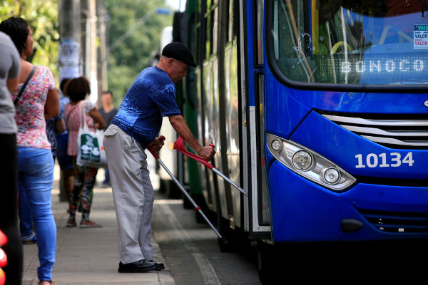 Homem idoso usando muletas para subir em ônibus, em texto sobre envelhecimento populacional no Brasil.