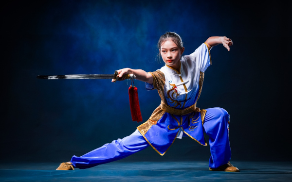 Mulher praticante de kung fu com roupa típica e em postura segurando espada. 