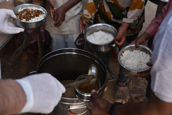 Pessoa distribuindo comida para pessoas em situação de pobreza. Na imagem, vê tigelas com arroz, feijão e carne.