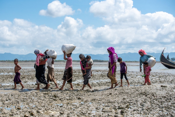 Grupo de refugiados deslocando-se sobre lama em razão de migração forçada.