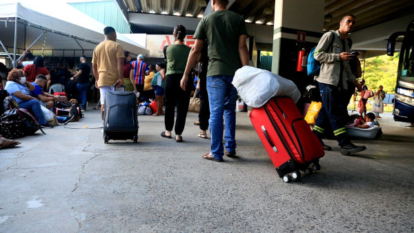 Pessoas segurando malas em rodoviária de Salvador, em referência à migração interna. 