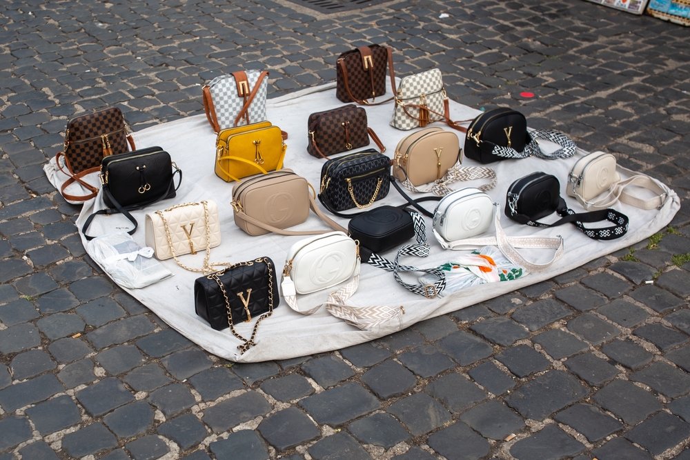 Bolsas falsificadas de diversas marcas dispostas no chão, um exemplo de pirataria.