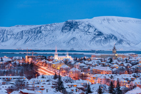 Vista noturna de uma montanha gelada e de uma cidade na Islândia, país insular da Eurásia.