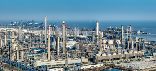 Uma grande refinaria de petróleo e complexo petroquímico localizados na costa sob um céu azul claro. 