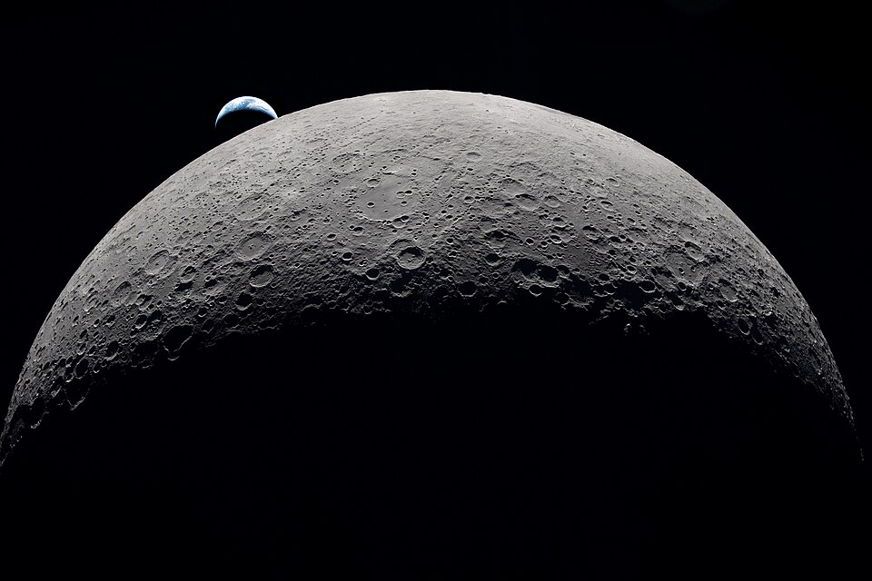 Imagem do lado oculto da Lua capturada pela missão Artemis II, com vislumbre do planeta Terra ao fundo.