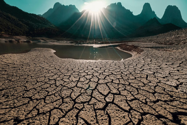 Solo rachado e reservatório seco diante de montanhas ao pôr do sol, ilustrando os impactos do super El Niño.