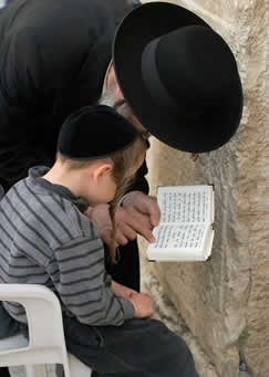 Judeu ortodoxo lendo texto sagrado com uma criança junto ao muro das lamentações