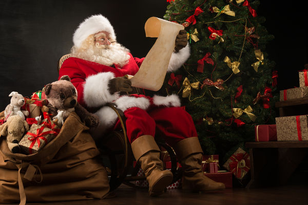 Papai Noel com um saco de presentes segurando um pergaminho.