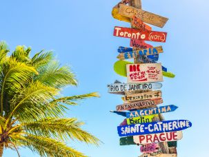 Tronco localizado na praia com várias placas com nome de destinos no sentido de sua localização.