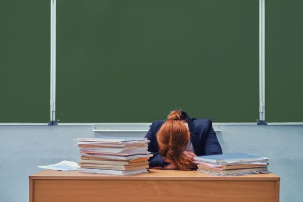 Professora cabisbaixa em sala de aula com problemas de saúde mental.