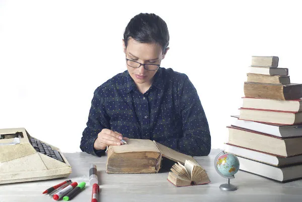 Mulher sentada a mesa rodeada de livros