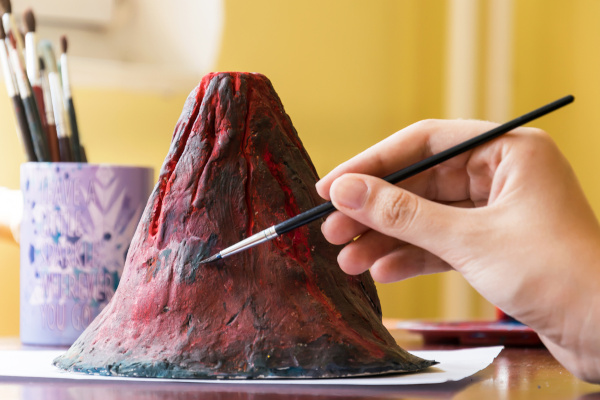 Pessoa pintando maquete de vulcão com tinta guache.