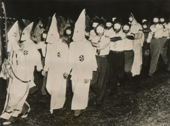 Homens da Ku Klux Klan com novos membros usando máscaras faciais.