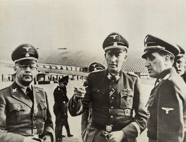 Na imagem estão Heinrich Himmler (à esquerda) e Reinhard Heydrich (no centro), os dois arquitetos da Solução Final.*