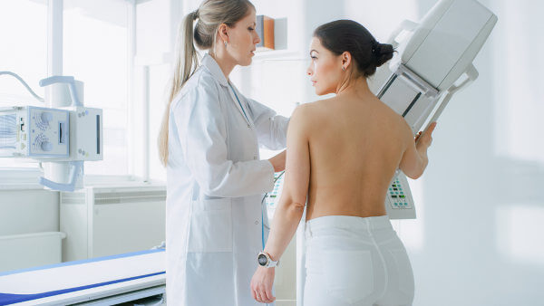 Mulher fazendo mamografia em referência ao câncer de mama.