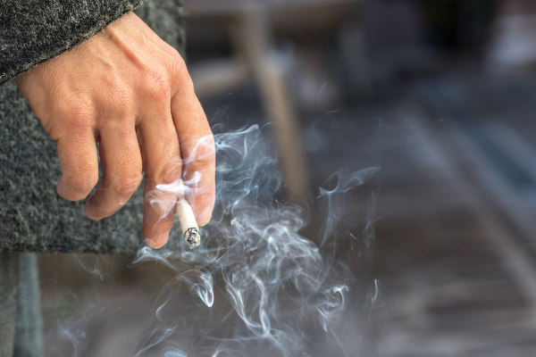 Pessoa com cigarro na mão em referência ao câncer.