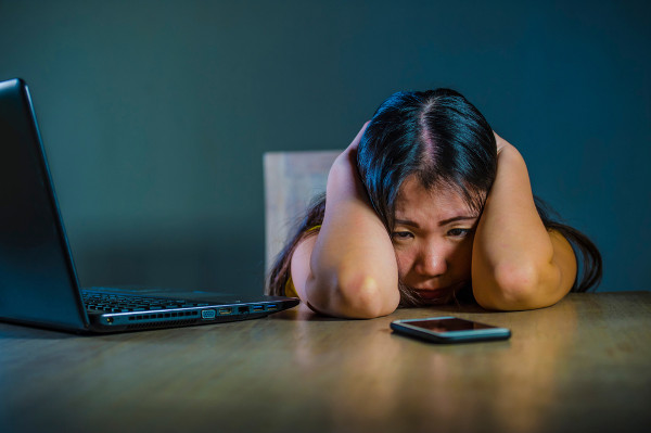 Menina com as duas mãos na cabeça e expressão de tristeza para representar as consequências do cyberbullying.