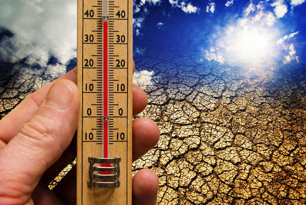 Pessoa segurando um termômetro e ao fundo um chão rachado em referência às mudanças climáticas.
