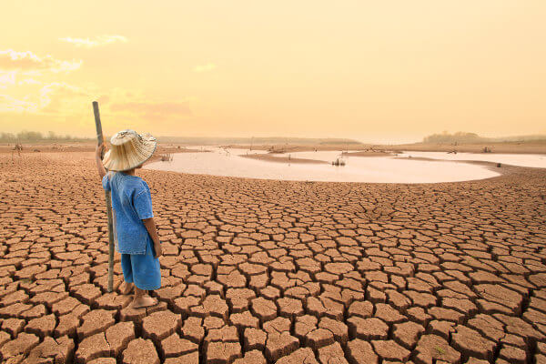 Criança em um chão rachado pelas secas em referência às mudanças climáticas