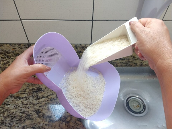 Mãos utilizando escorredor de arroz, uma invenção brasileira.