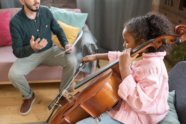 professor e aluna criança tocando violoncelo
