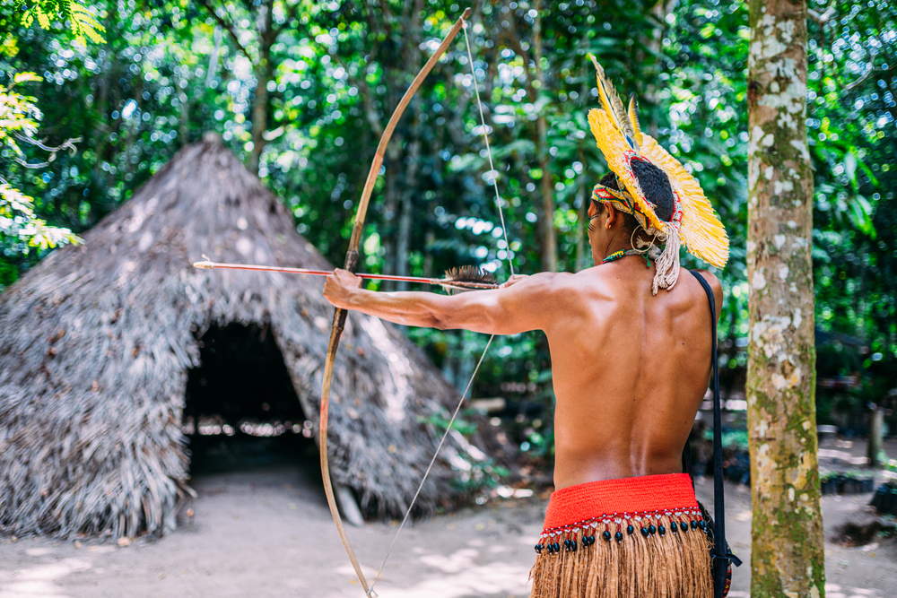 Homem indígena atira arco e flecha de costas
