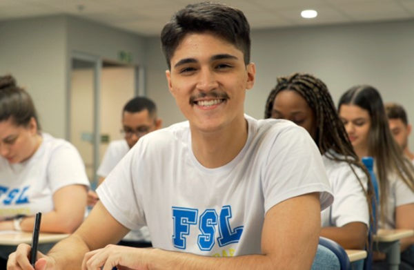 Imagem do aluno Pedro, do curso de Fisioterapia, sorrindo dentro de uma sala de aula.