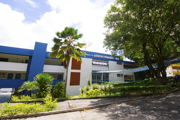 Fundo laranja, listras cinza e preto. Foto da entrada do campus da Uneb com pessoas andando. Texto Vestibular 2024 Uneb